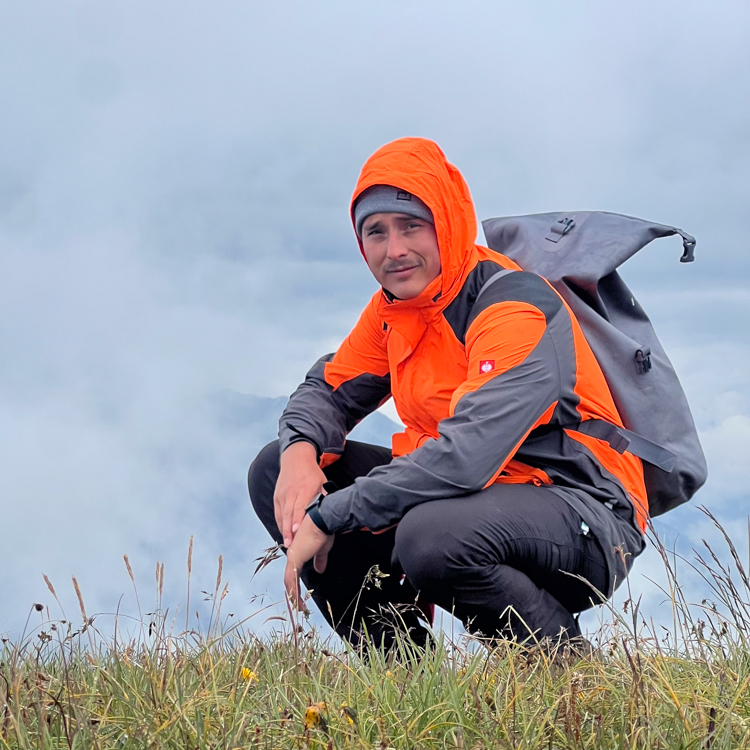 Pablo outdoors in the mountains, wearing an orange hiking jacket